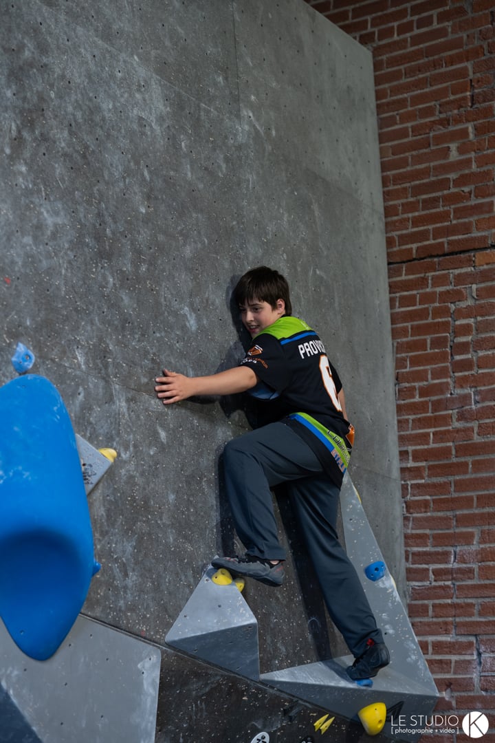 A smiling boy in a club jersey climbs a slab.