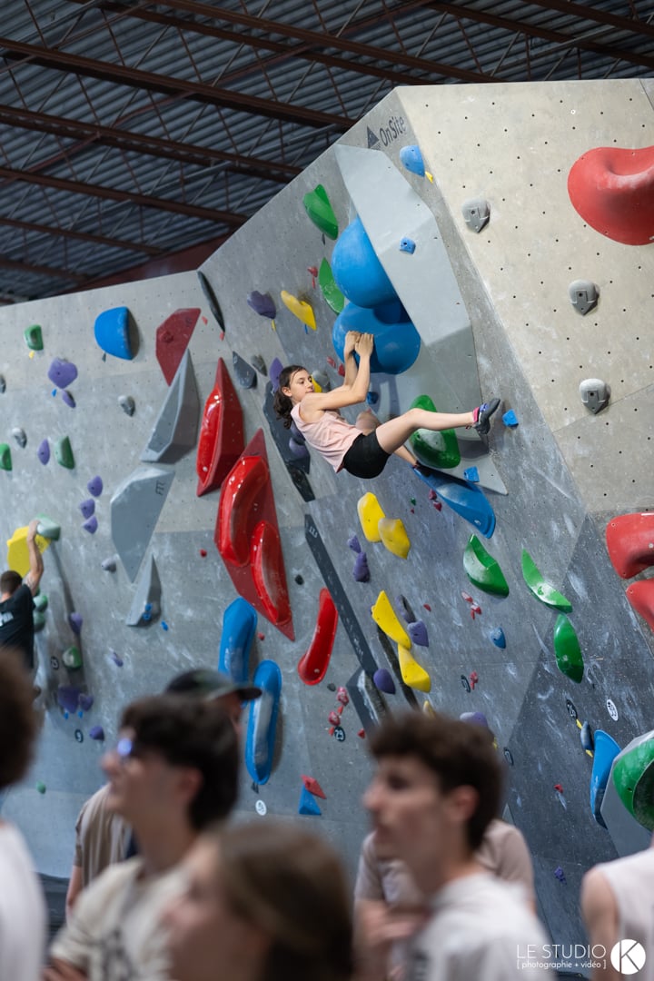 A young climber mid-move on a large, colourful bouldering wall