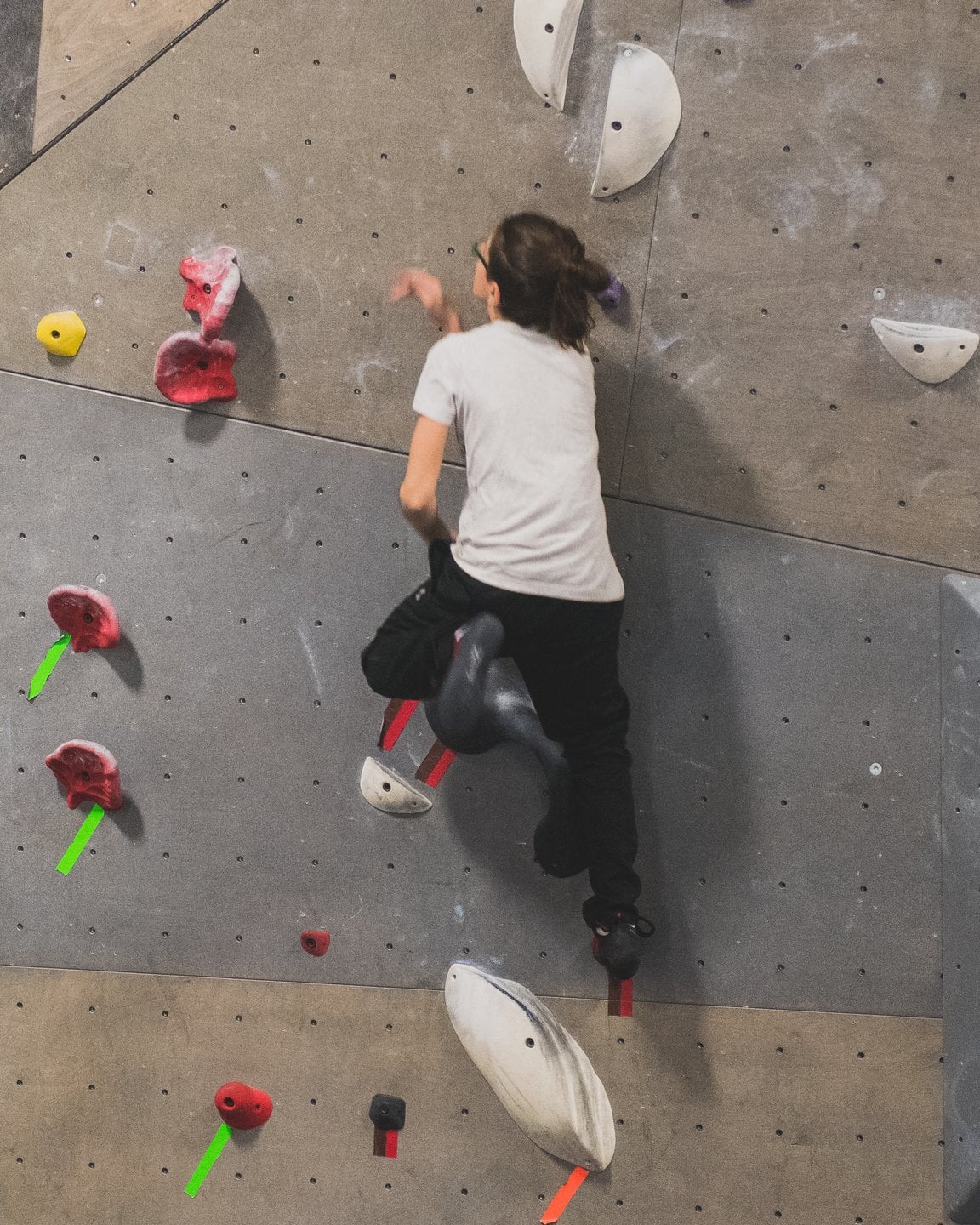 Un enfant en plein mouvement sur le mur, une main tendue vers la prochaine prise