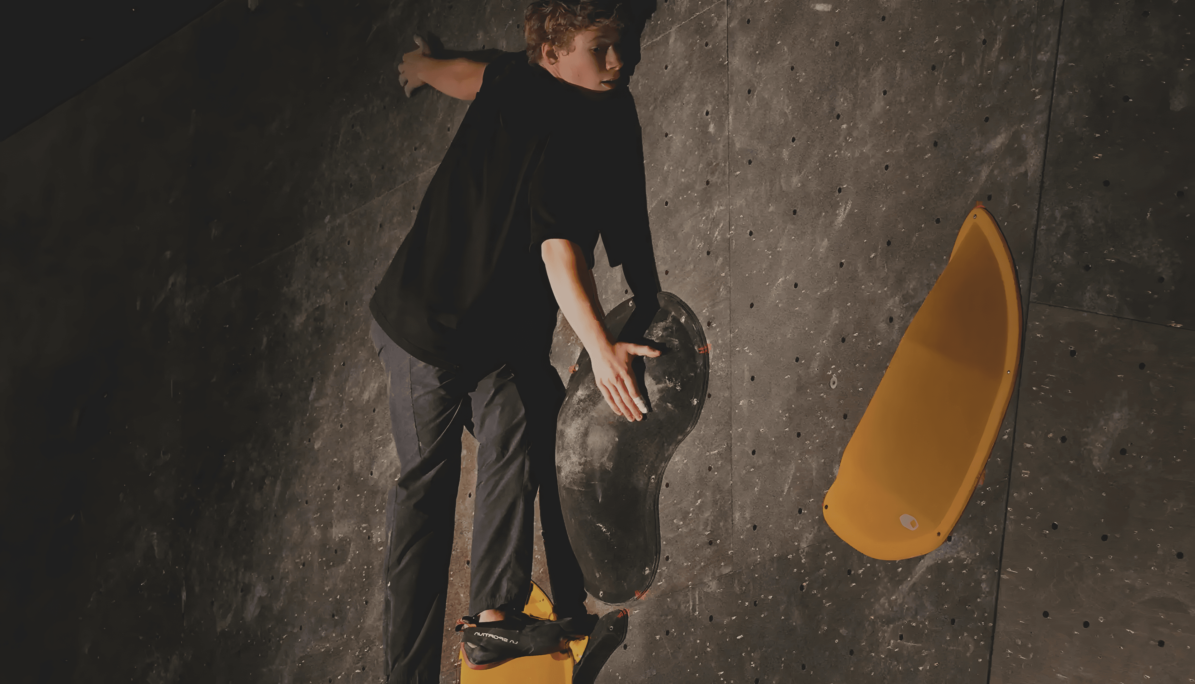 Climber on an indoor bouldering wall, hand reaching for a hold